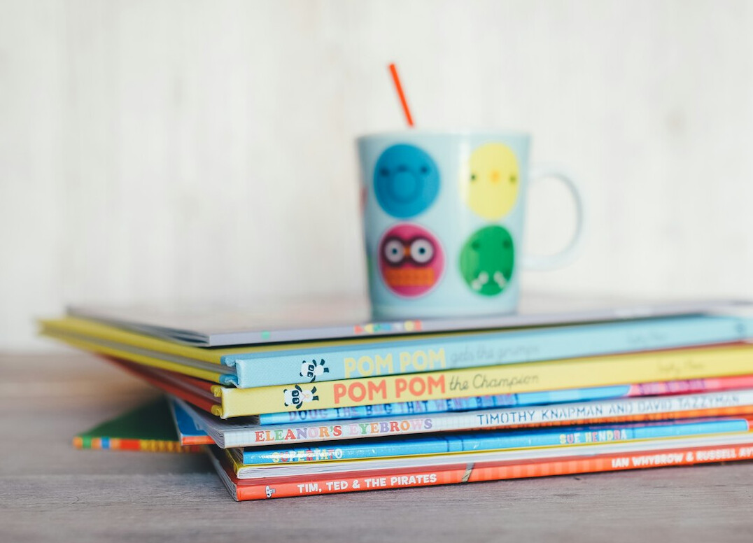 Stack of colourful books with reading glasses on a table